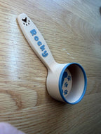 Cream personalized dog food scoop printed with the name Rocky, showing the paw print detail