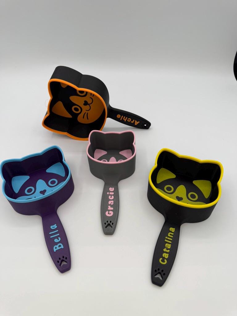 Personalized cat food scoops in several colors, each printed with a different cat's name